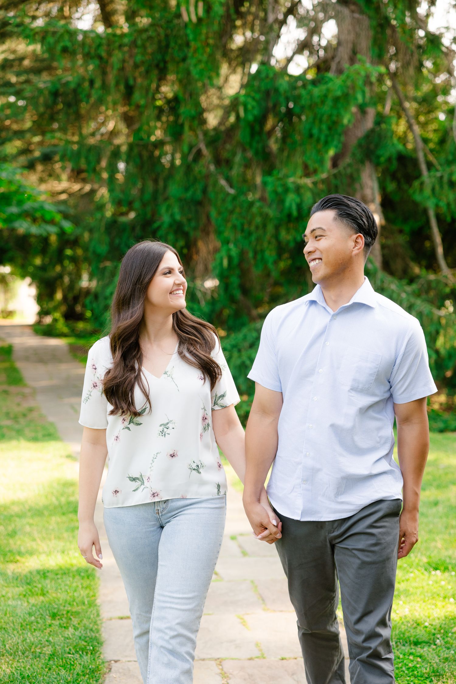 A couple walks together on a stone path while sharing a loving glance in a serene garden setting.