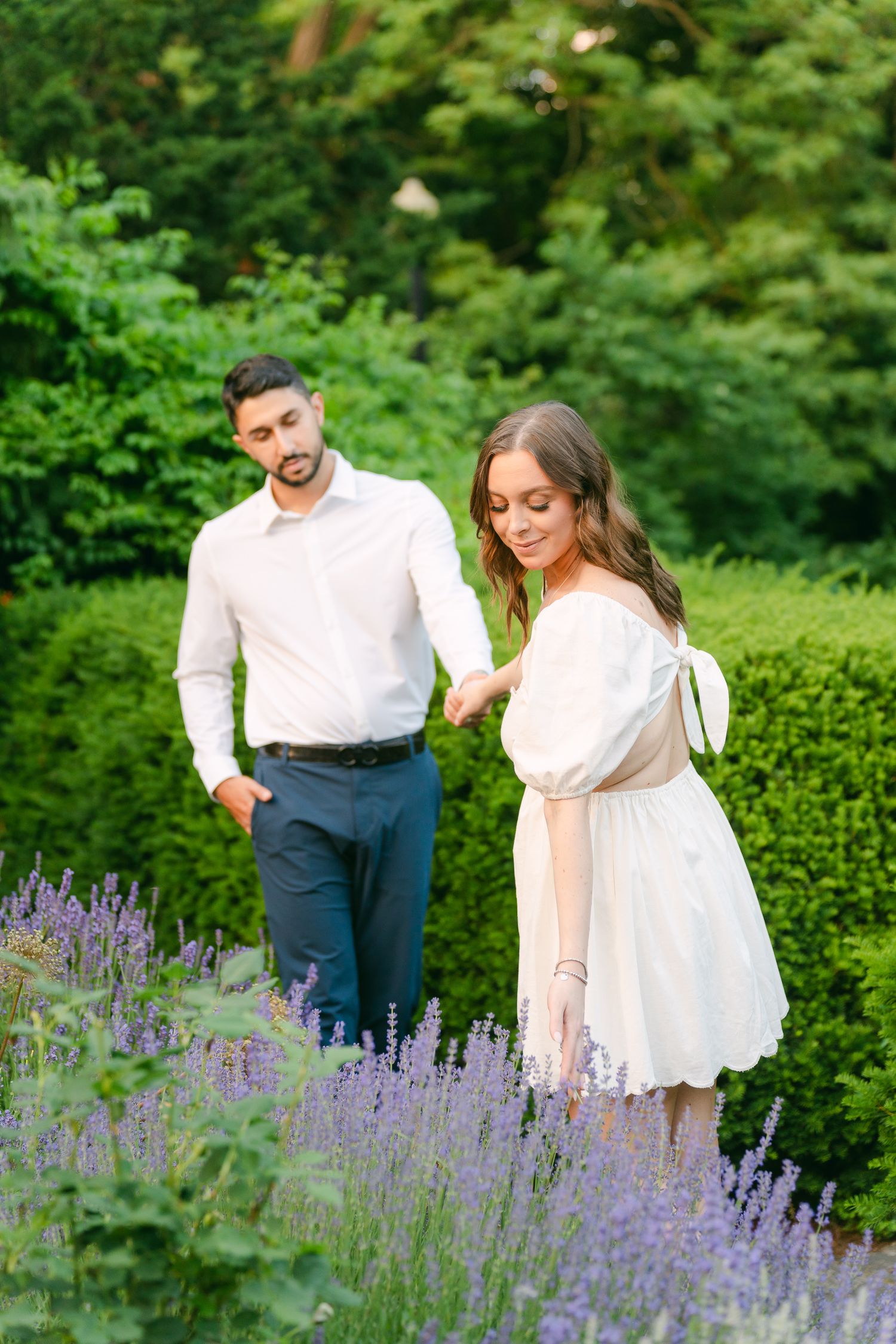 A couple walks through a beautiful garden with lavender blooms and manicured hedges.