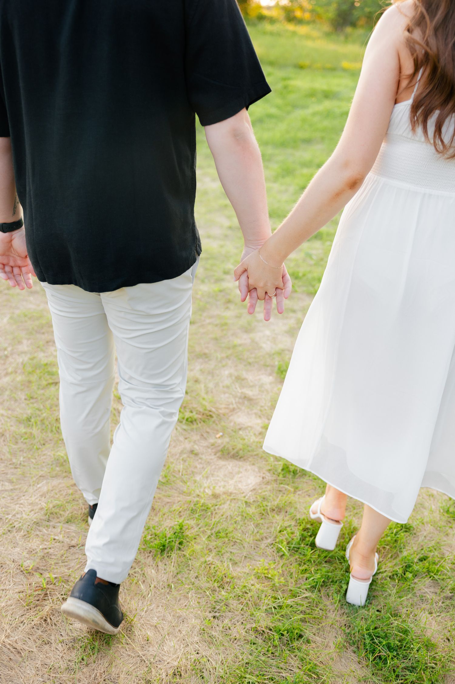 Close-up view of couple walking hand in hand on grass path in summer.