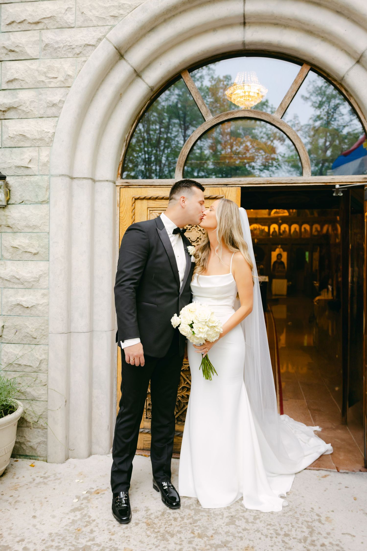 A romantic moment between newlyweds under an elegant stone archway at their church wedding.