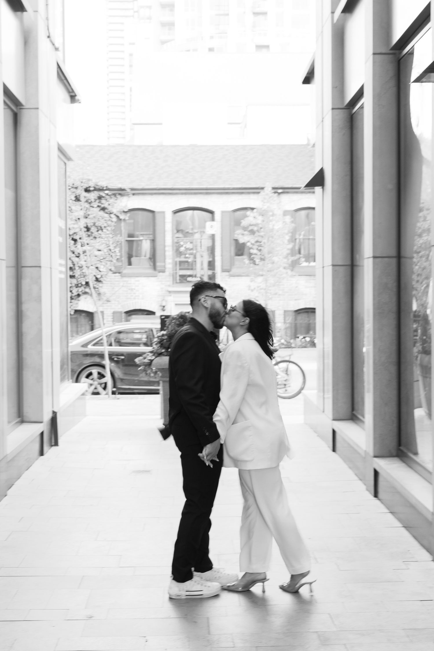 A black and white photo of a couple sharing an intimate moment in a modern hallway.