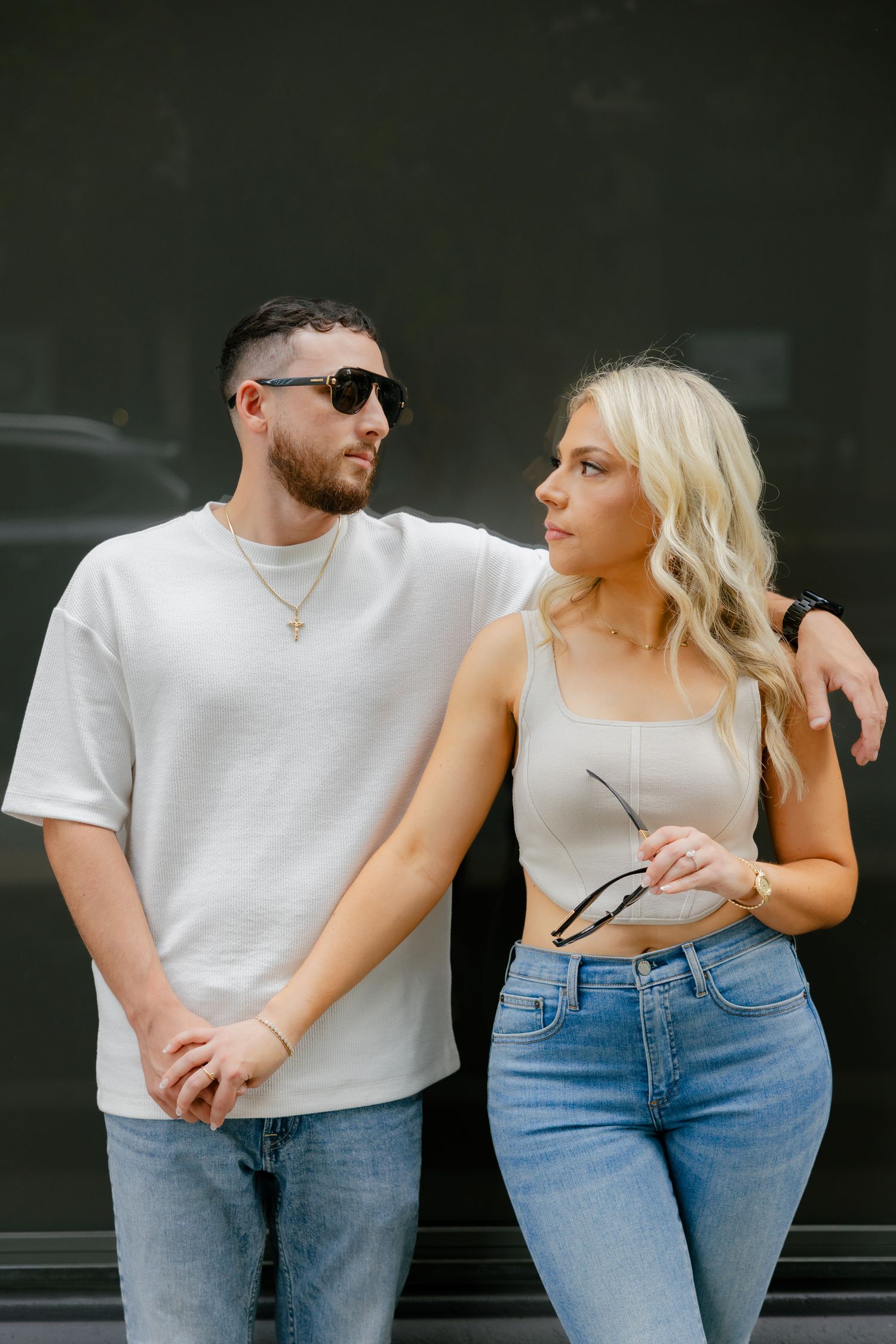 Contemporary couple in complementary outfits pose against dark urban background.