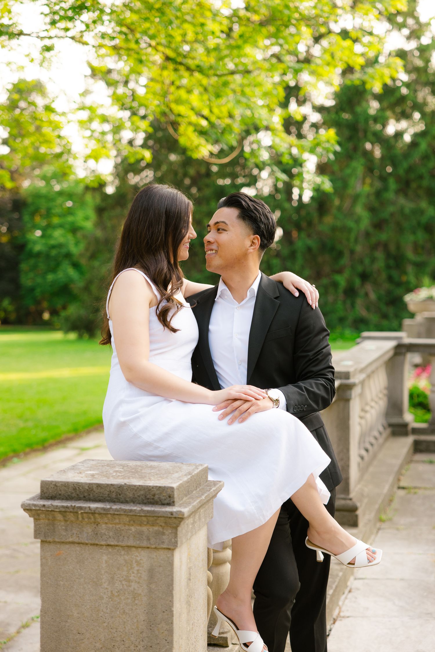 Intimate portrait of couple sharing tender moment on stone railing with sunlit garden backdrop.