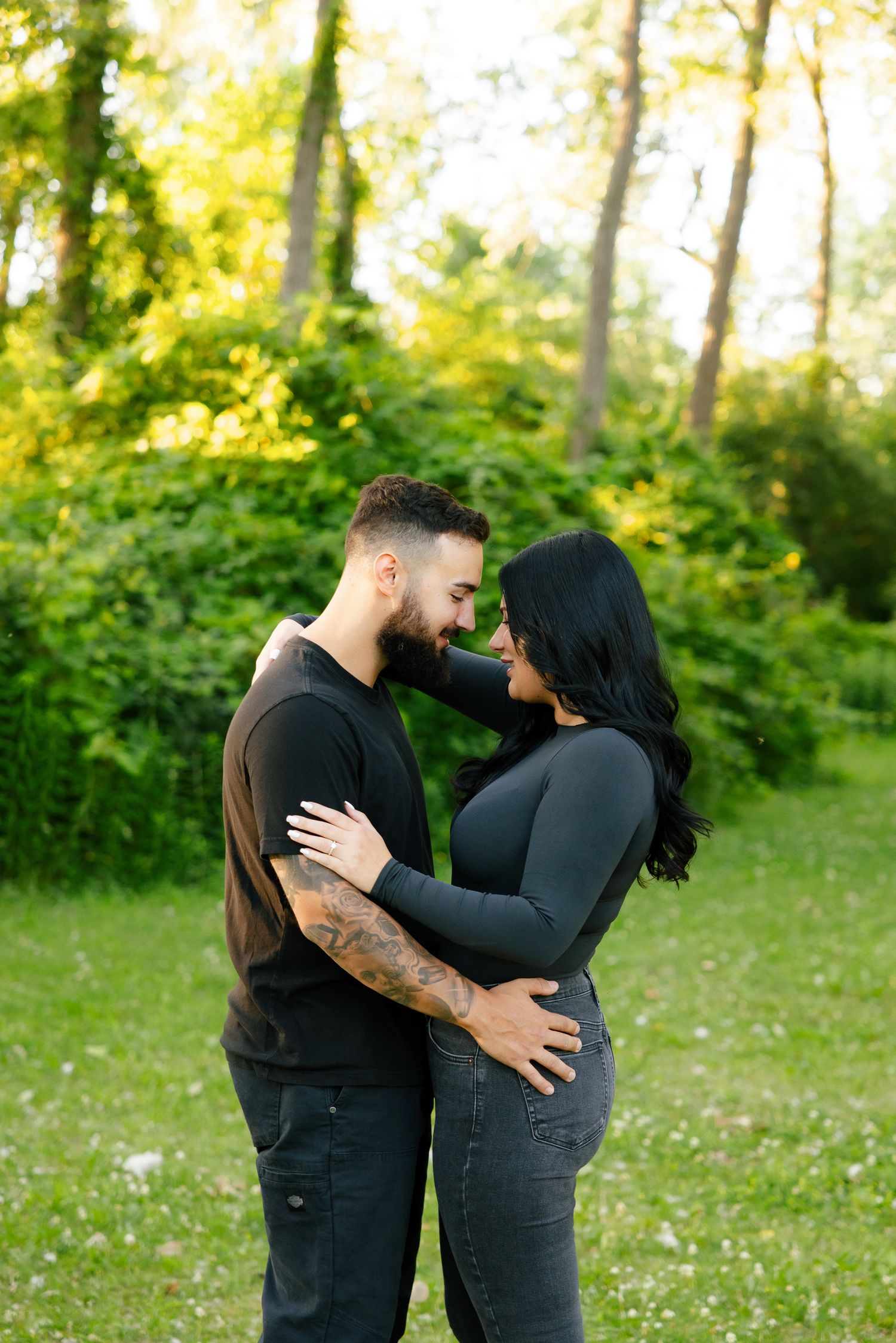 A couple shares an intimate moment while embracing outdoors in a wooded setting with golden sunlight.