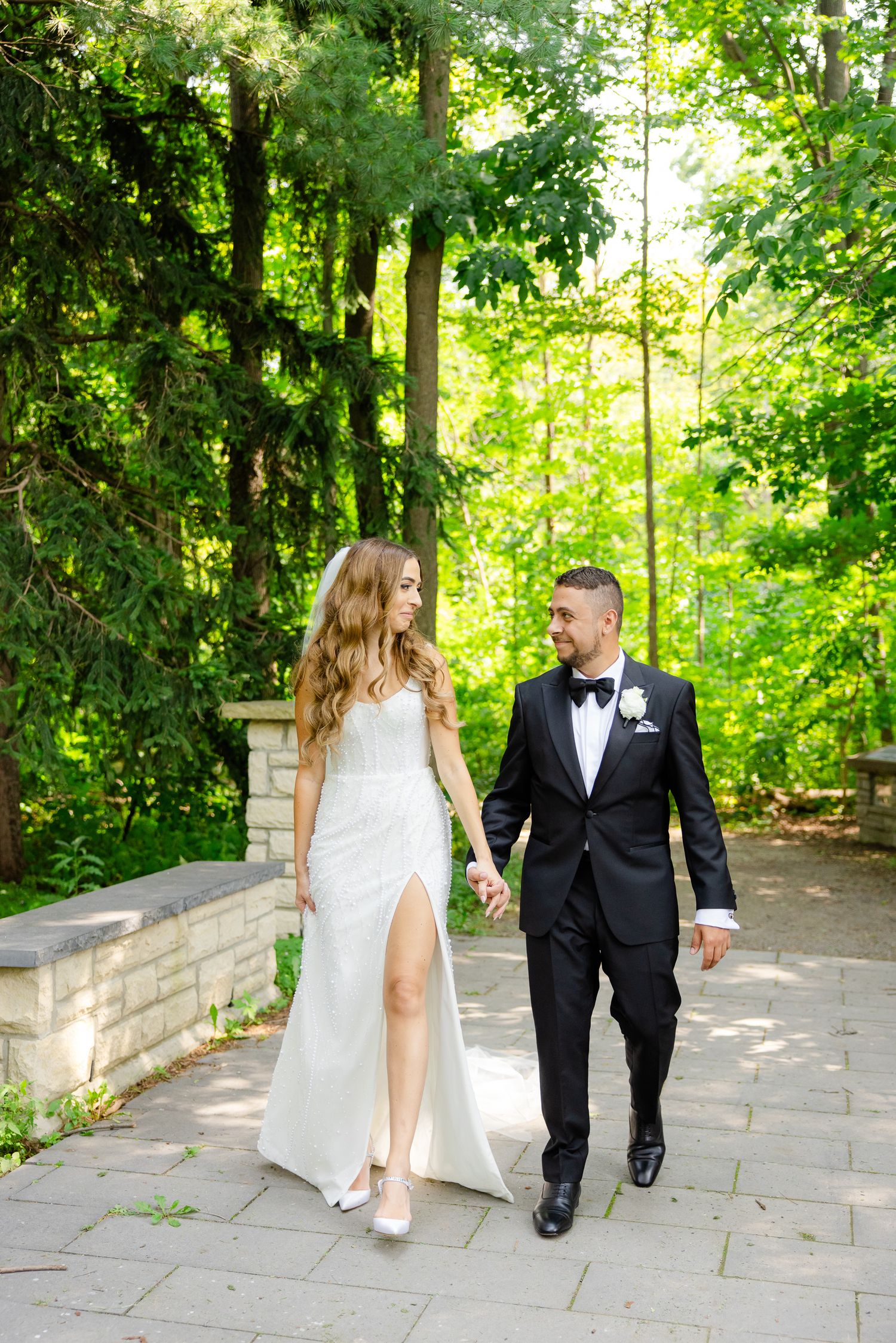 Wedding couple strolling together on stone pathway surrounded by bright green summer forest.