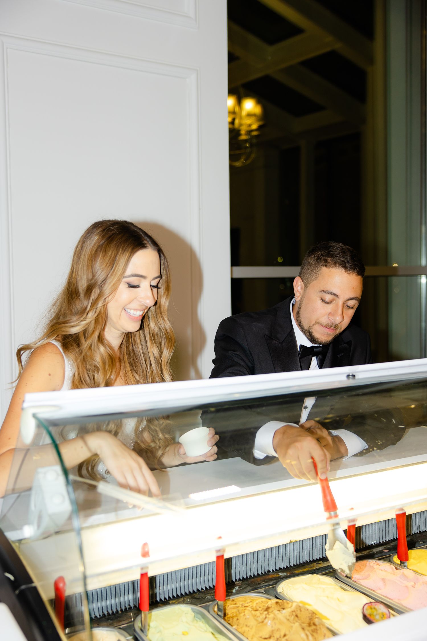 Wedding couple selecting flavors from an elegant gelato cart at an indoor reception.
