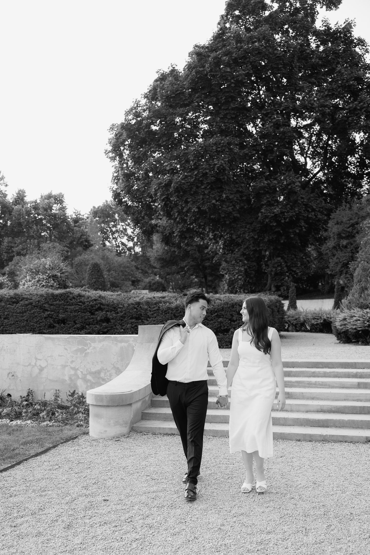 A black and white photo of a couple strolling along a gravel path near stone steps.