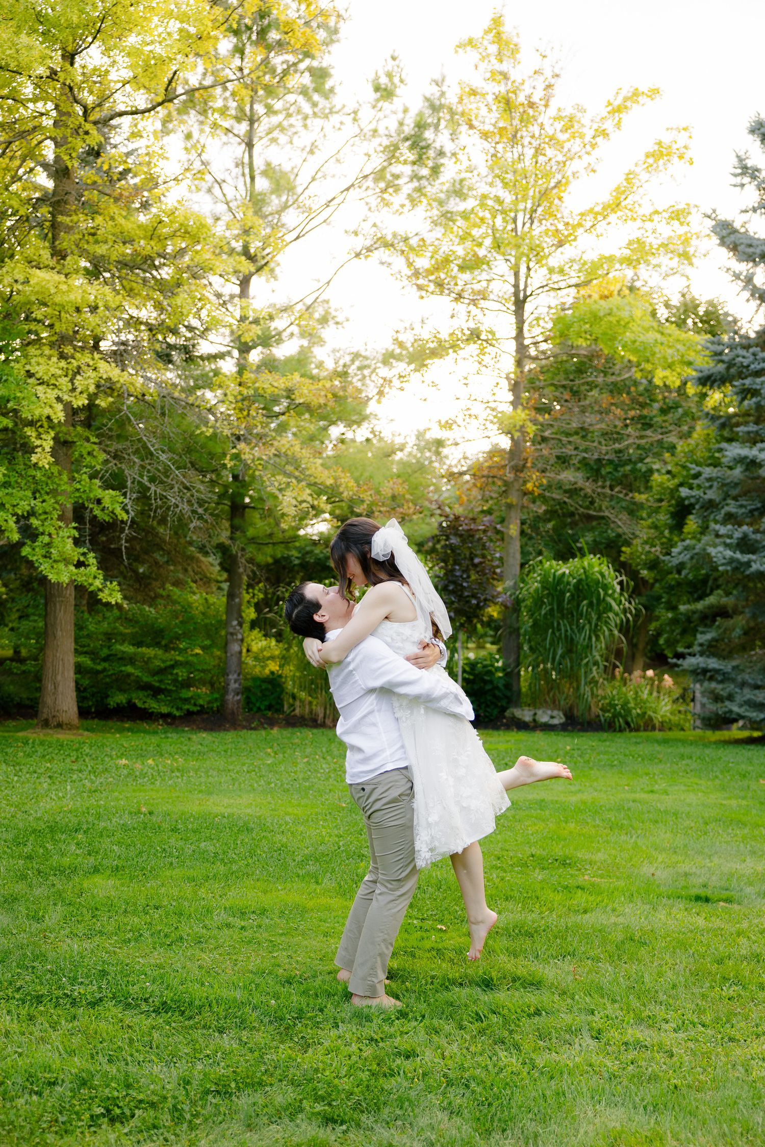 Romantic lift pose in a garden setting with sunlit trees creating a natural backdrop.