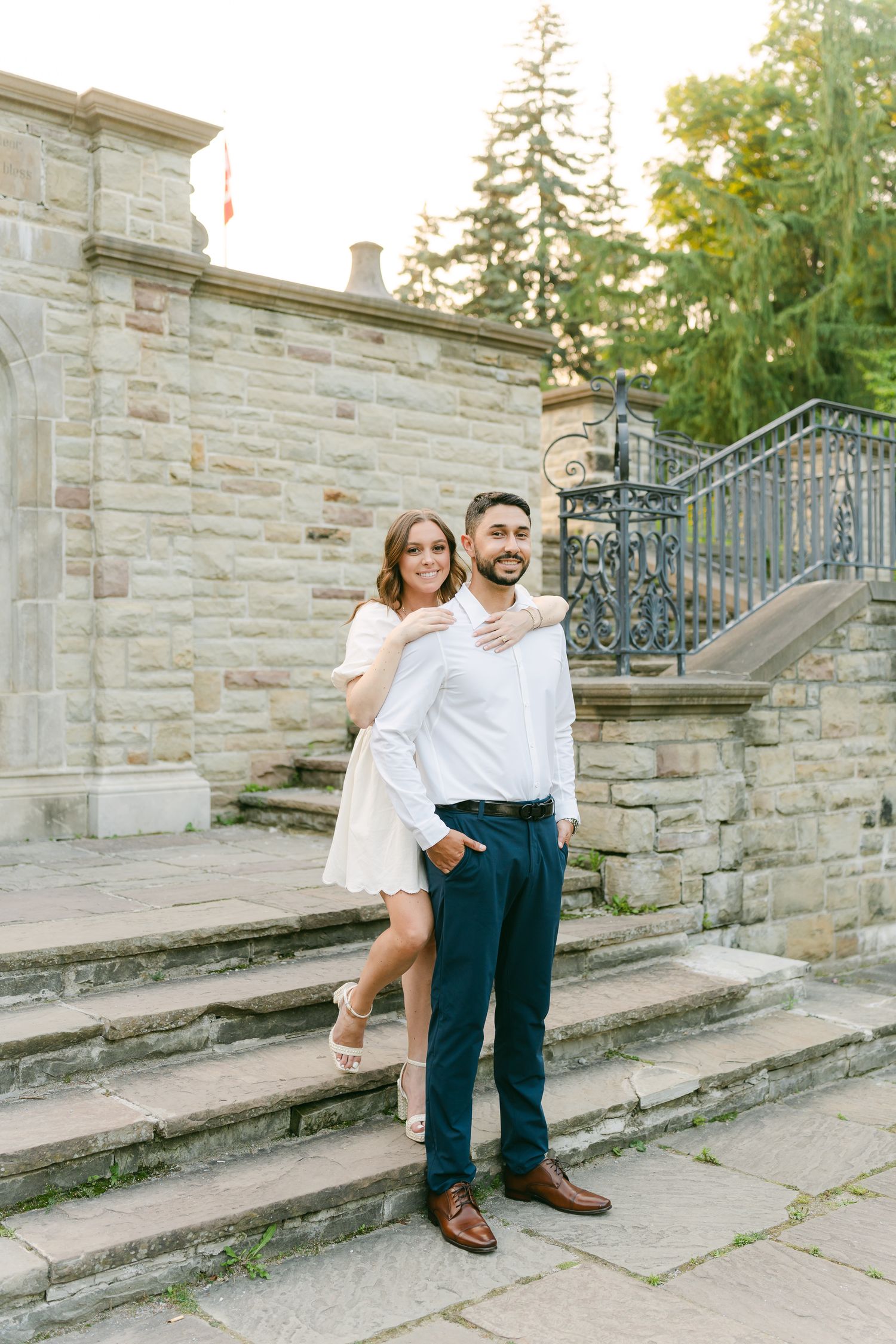 A romantic engagement photoshoot on stone steps featuring coordinated white and navy outfits against a classic architectural backdrop.
