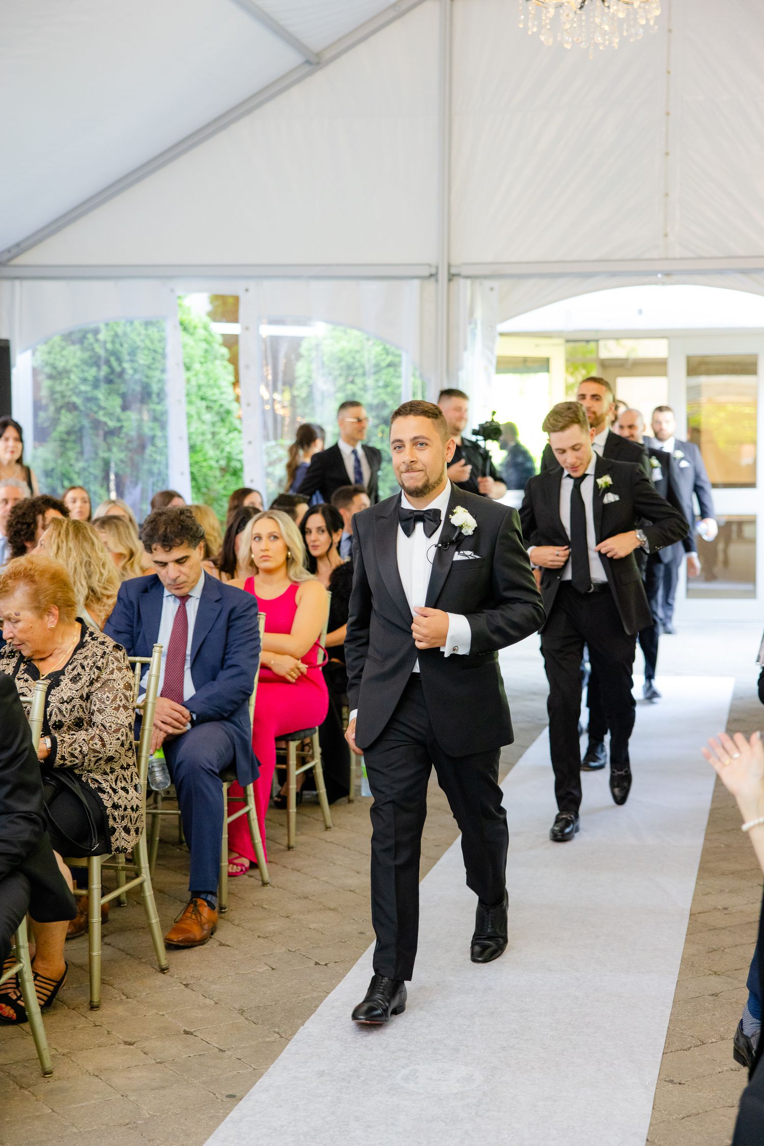 Wedding party members make their entrance at a tented reception venue with elegant chandelier lighting.