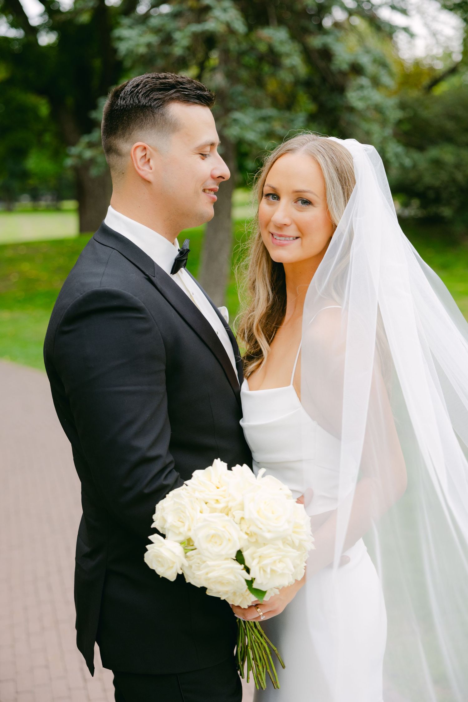 Elegant wedding portrait in garden setting with white floral bouquet and flowing veil.