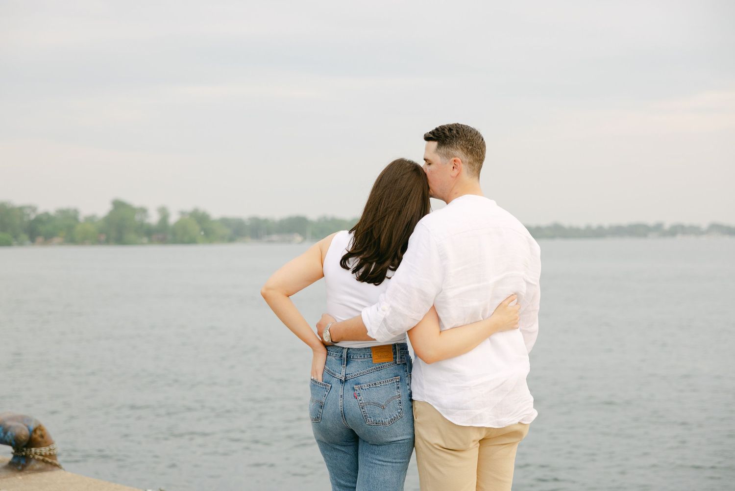 Couple embracing while looking out over waterfront from wooden pier.