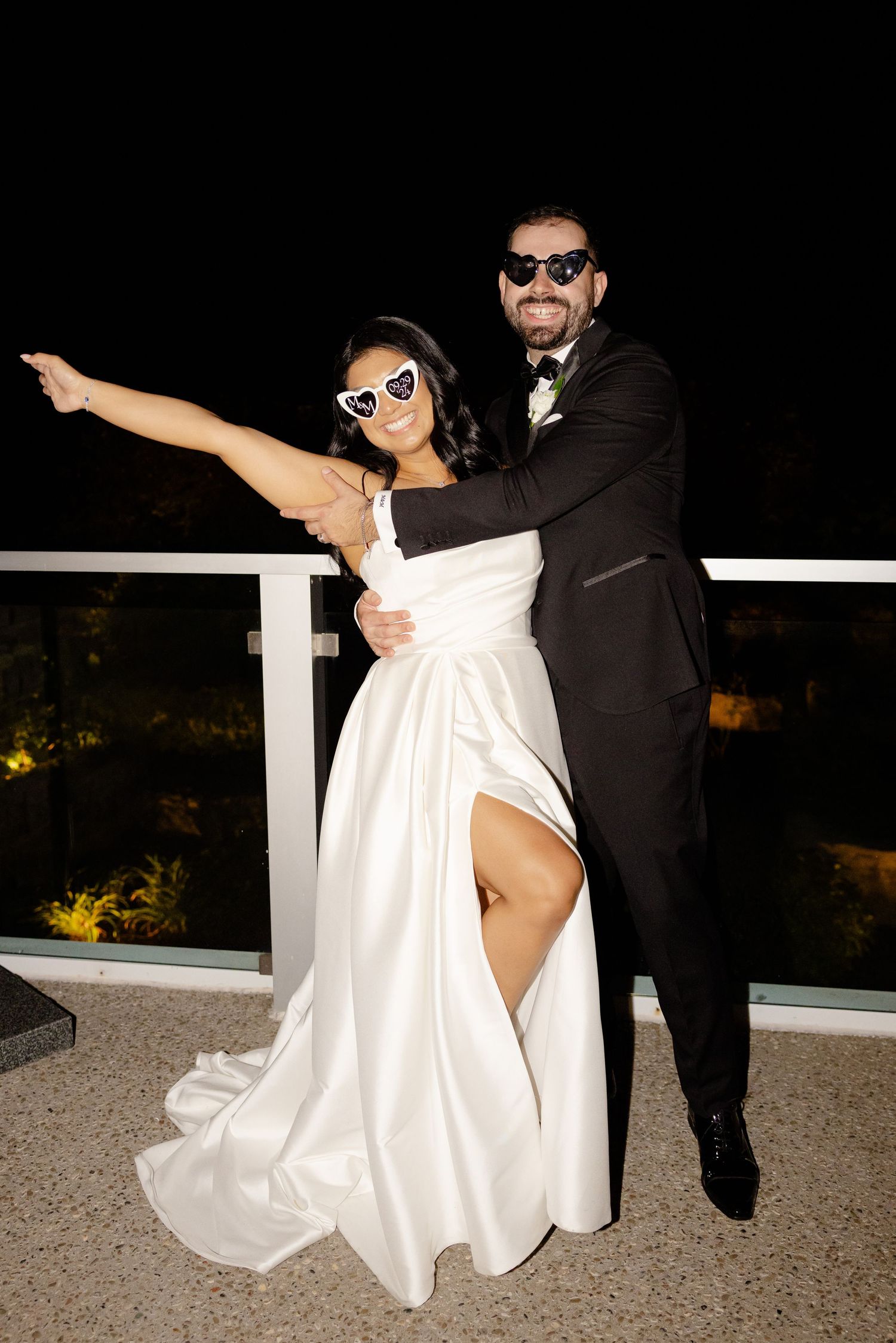 Fun wedding portrait of couple striking dramatic pose in sunglasses on balcony.