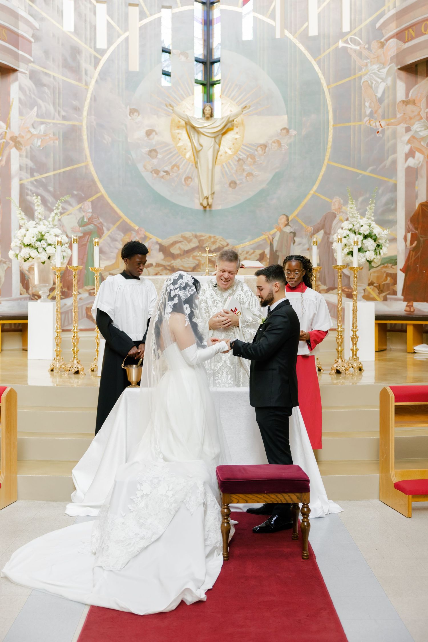 A wedding ceremony taking place in a church with ornate decor and white floral arrangements.