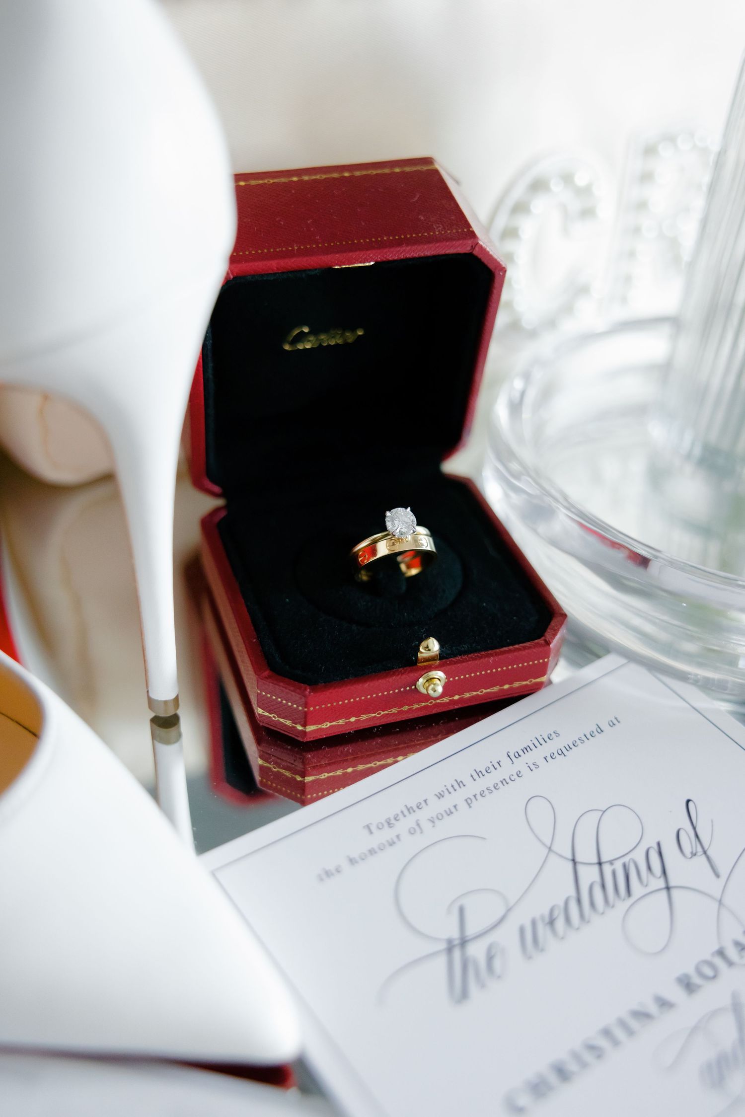 Diamond engagement ring in red Cartier box displayed with wedding invitation details.