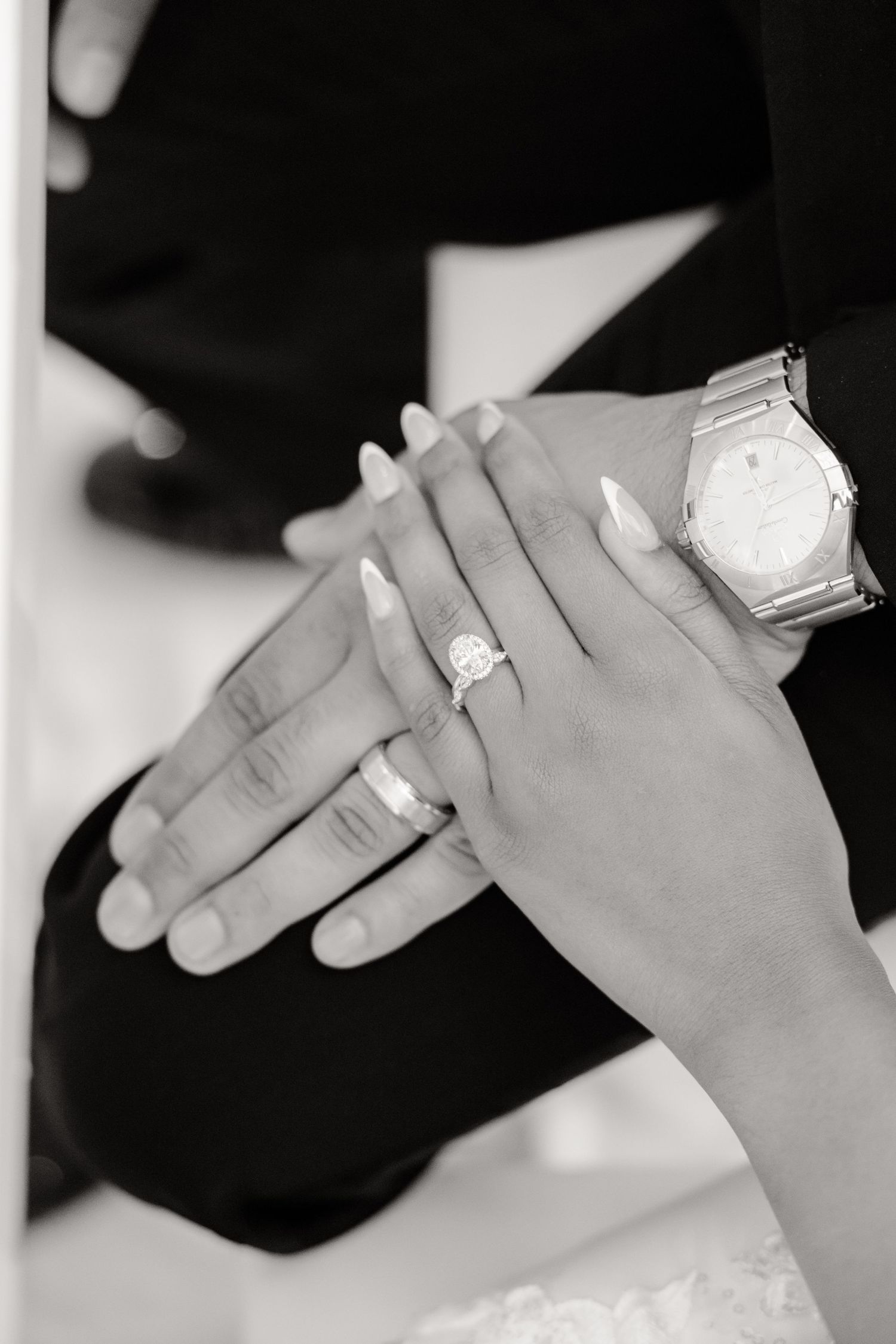 Close-up black and white photo of hands showing elegant engagement ring and watch details.