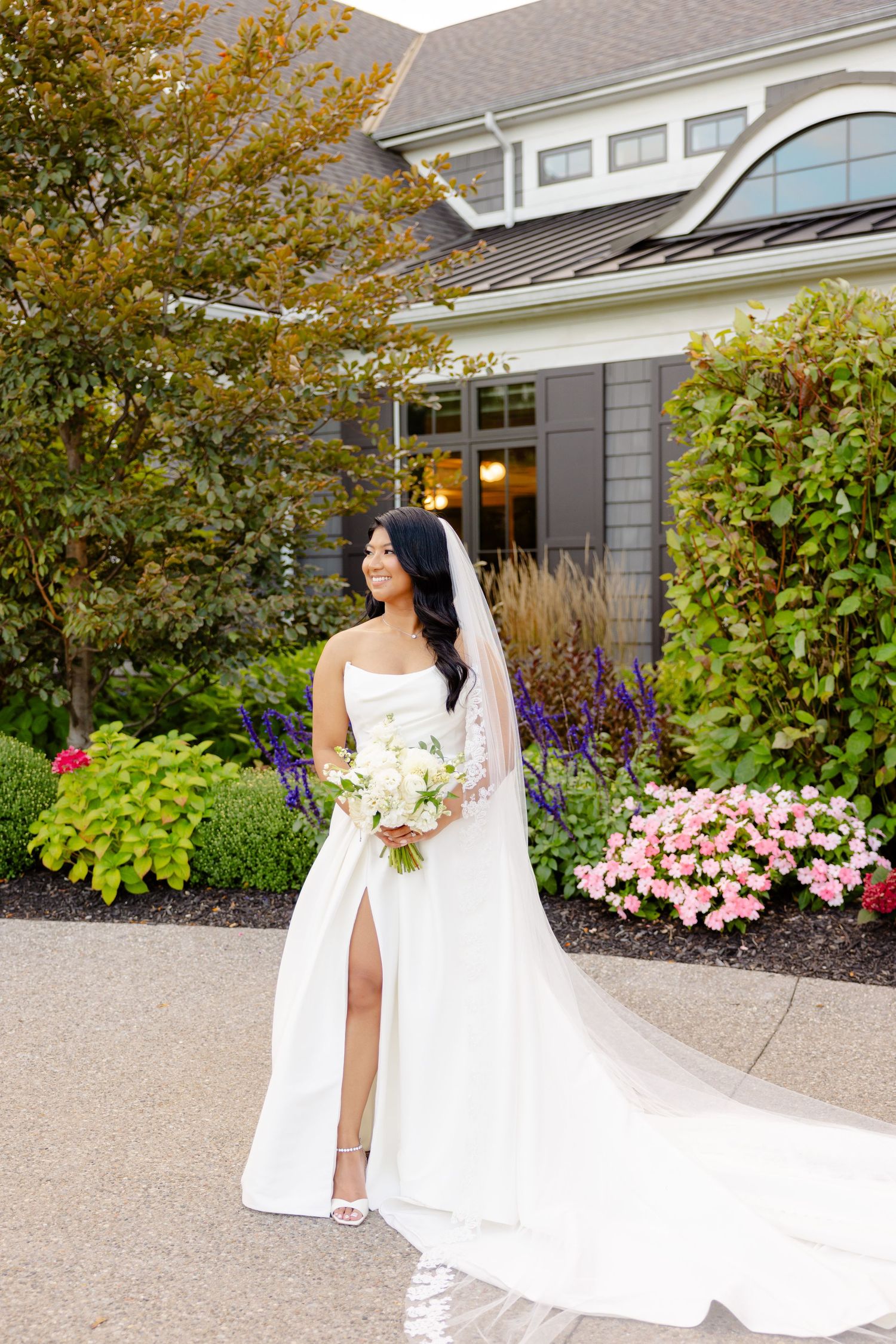 Wedding photography featuring a modern white gown with side slit against grey house and autumn foliage.