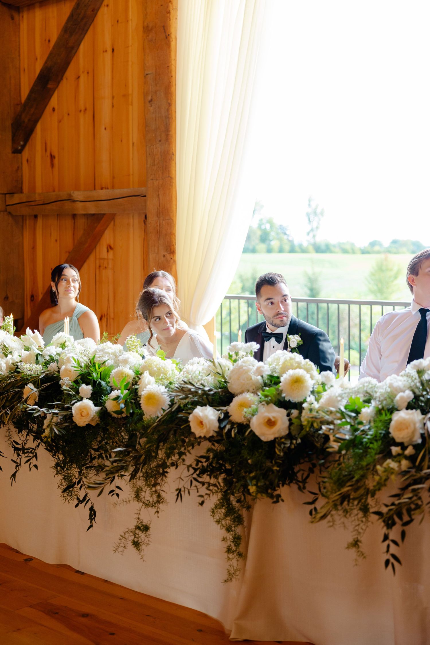 Elegant head table with lush white floral arrangements in a rustic barn wedding venue.