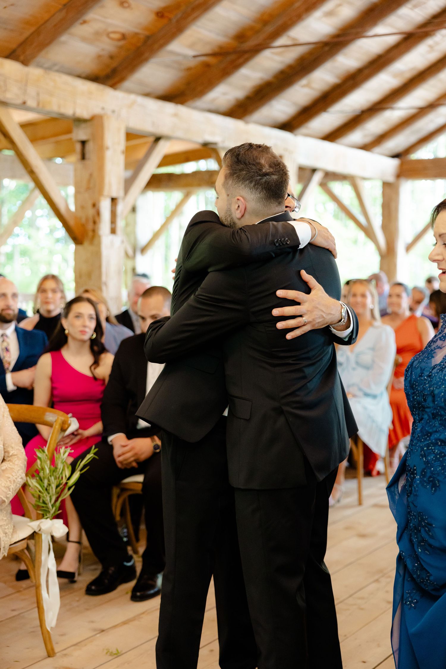 Emotional embrace during wedding ceremony in wooden pavilion with guests watching.