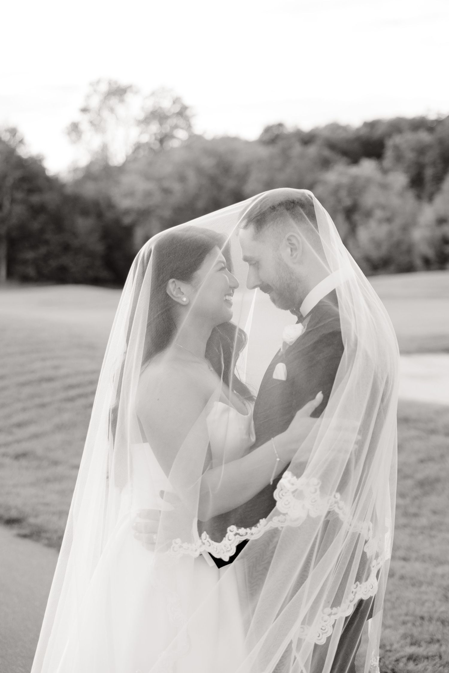 Black and white intimate wedding portrait with couple embracing under flowing veil.