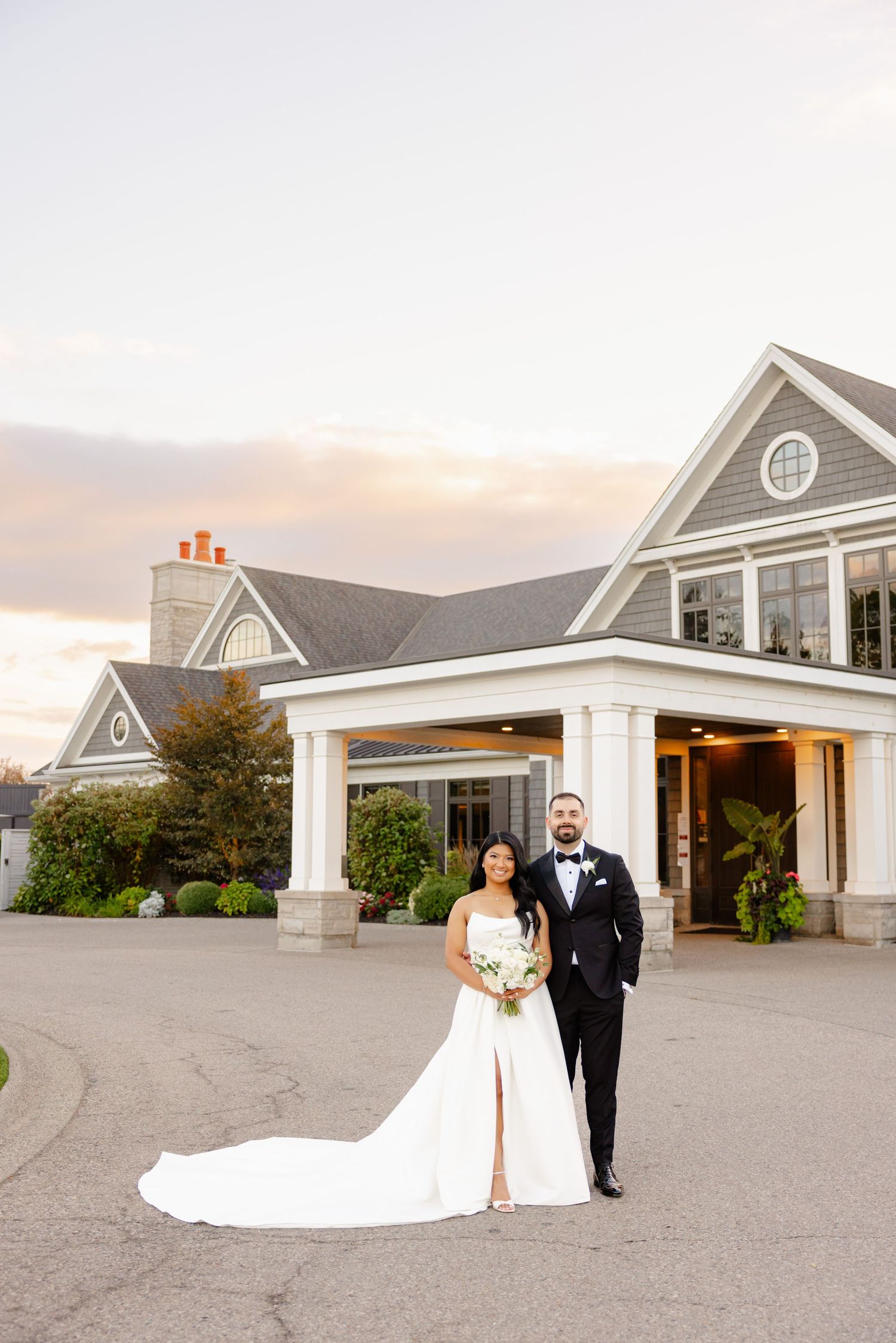 An elegant wedding portrait in front of a grand country club entrance at sunset.