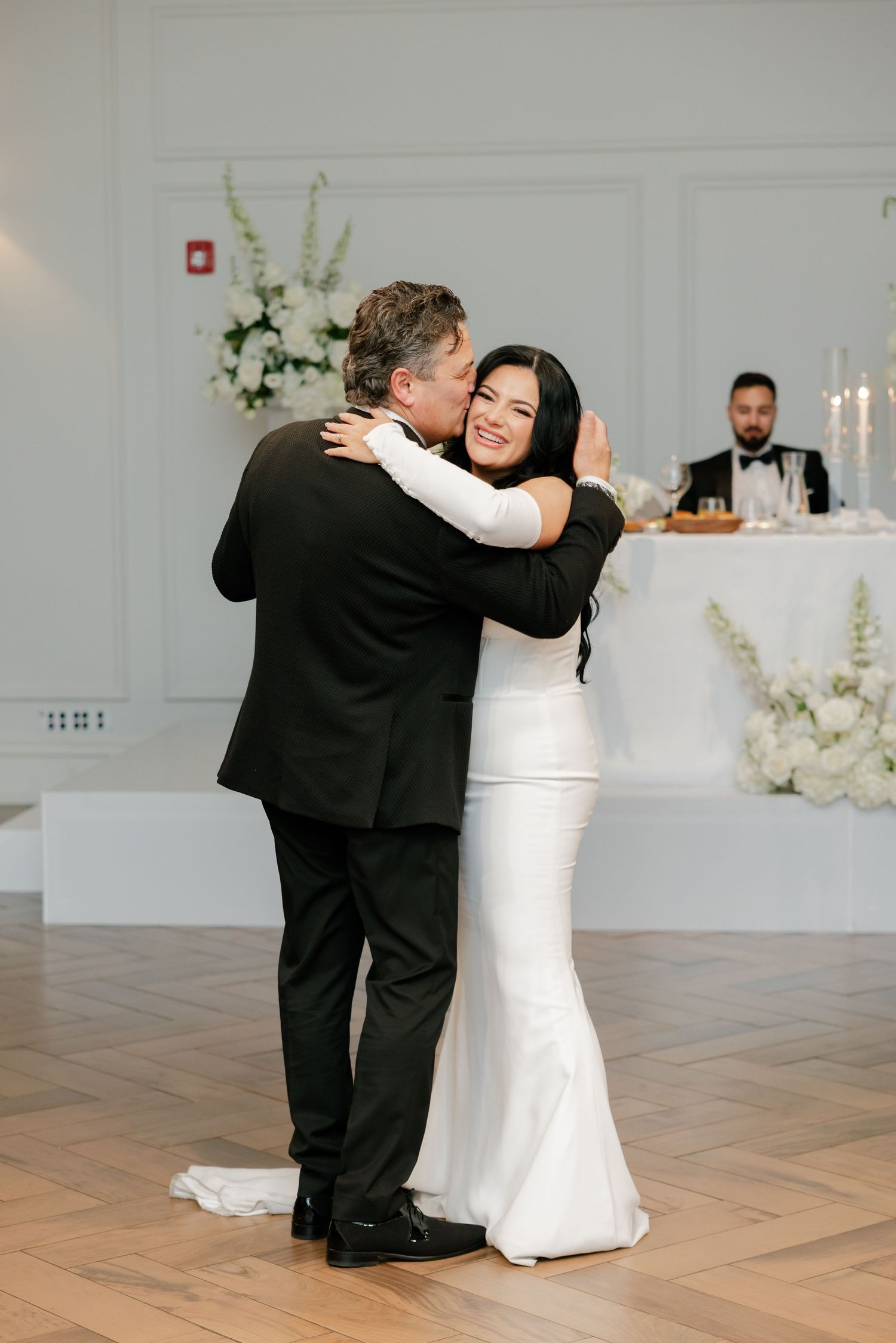 A tender dance moment captured during a wedding reception with elegant white decor.