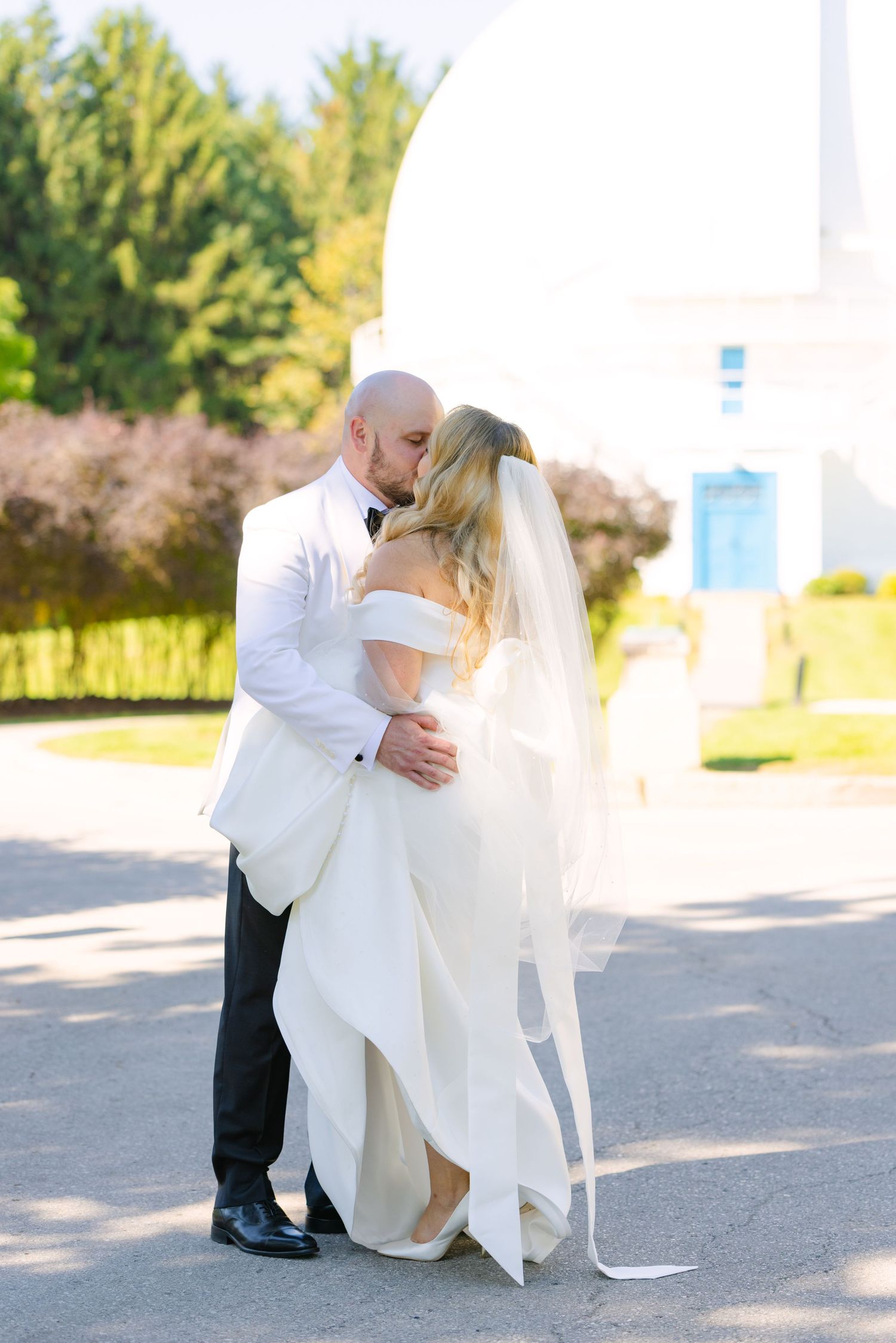 Romantic outdoor wedding portrait with flowing white dress and veil against natural backdrop.