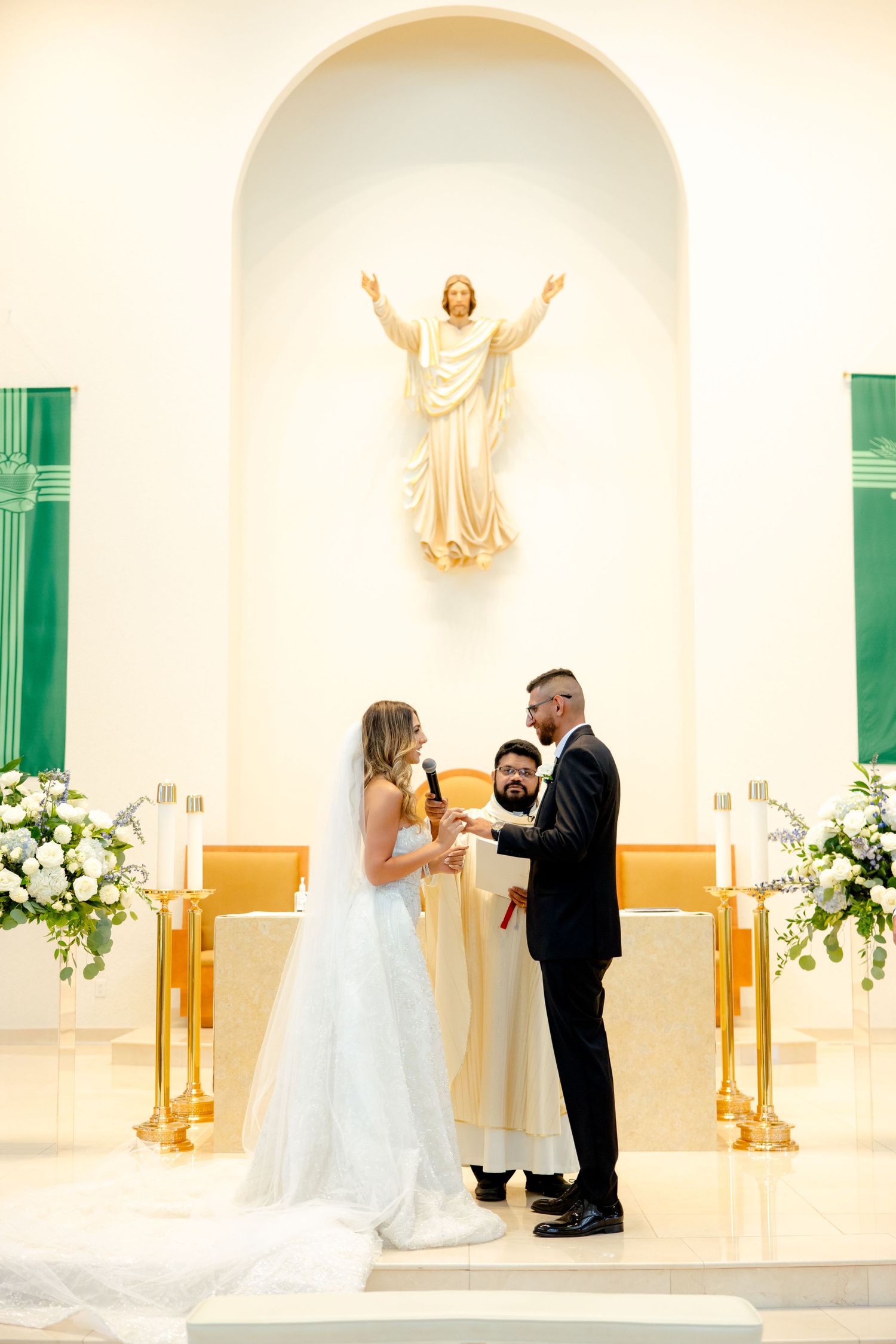 Wedding ceremony moment beneath religious statue with gold accents and white floral decorations.