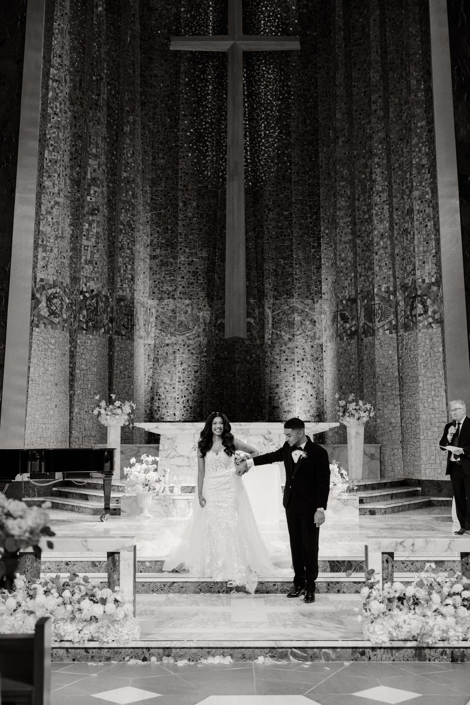 A black and white photo of newlyweds celebrating at the altar of a grand church.
