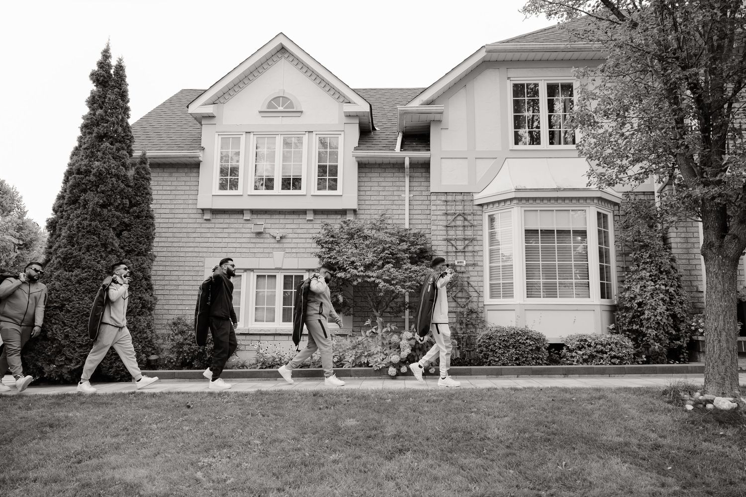 Several people walk across the lawn of a large two-story suburban house.