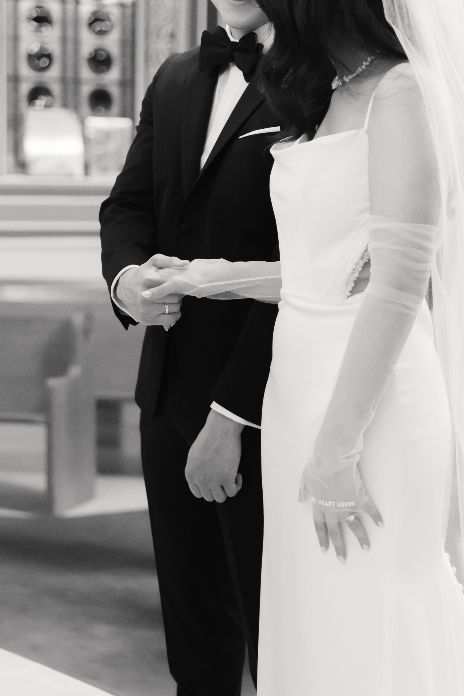 Black and white closeup of formal wedding attire during ceremony exchange.