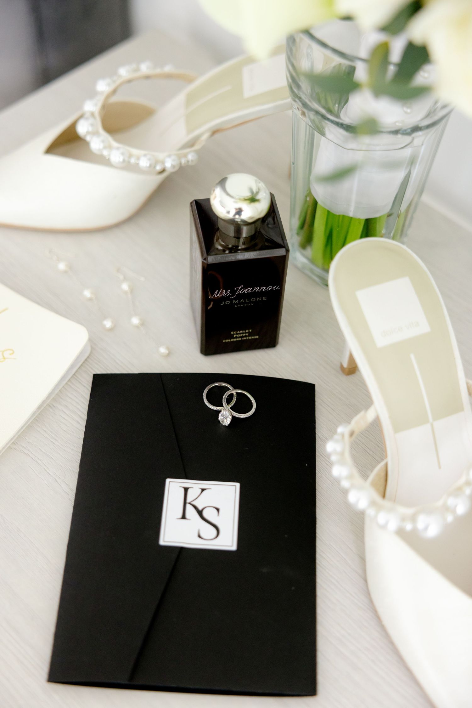 Wedding accessories including white heels, rings, and black invitation with KS monogram.