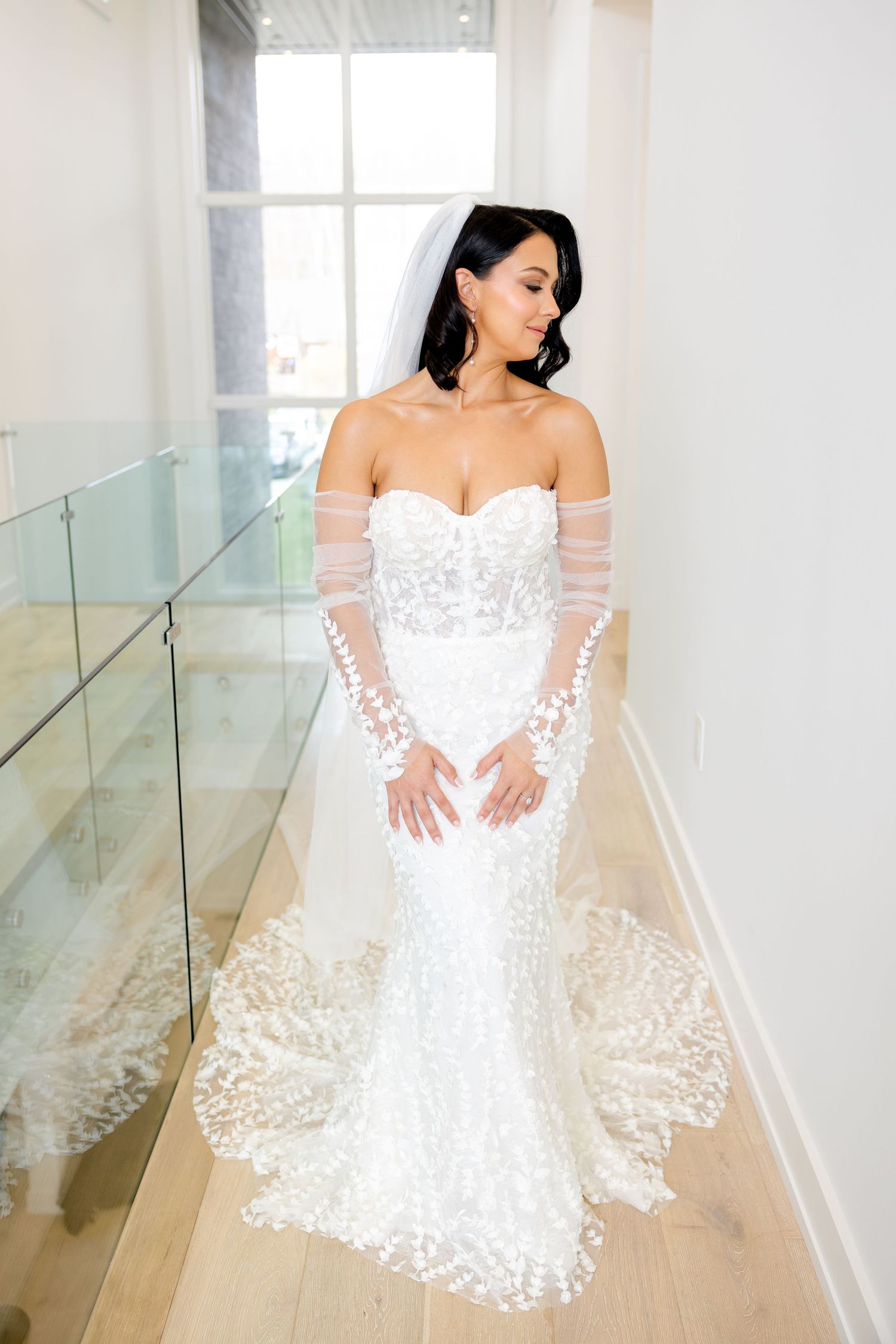 Full length view of bride in fitted lace wedding dress with long train in modern bright corridor.