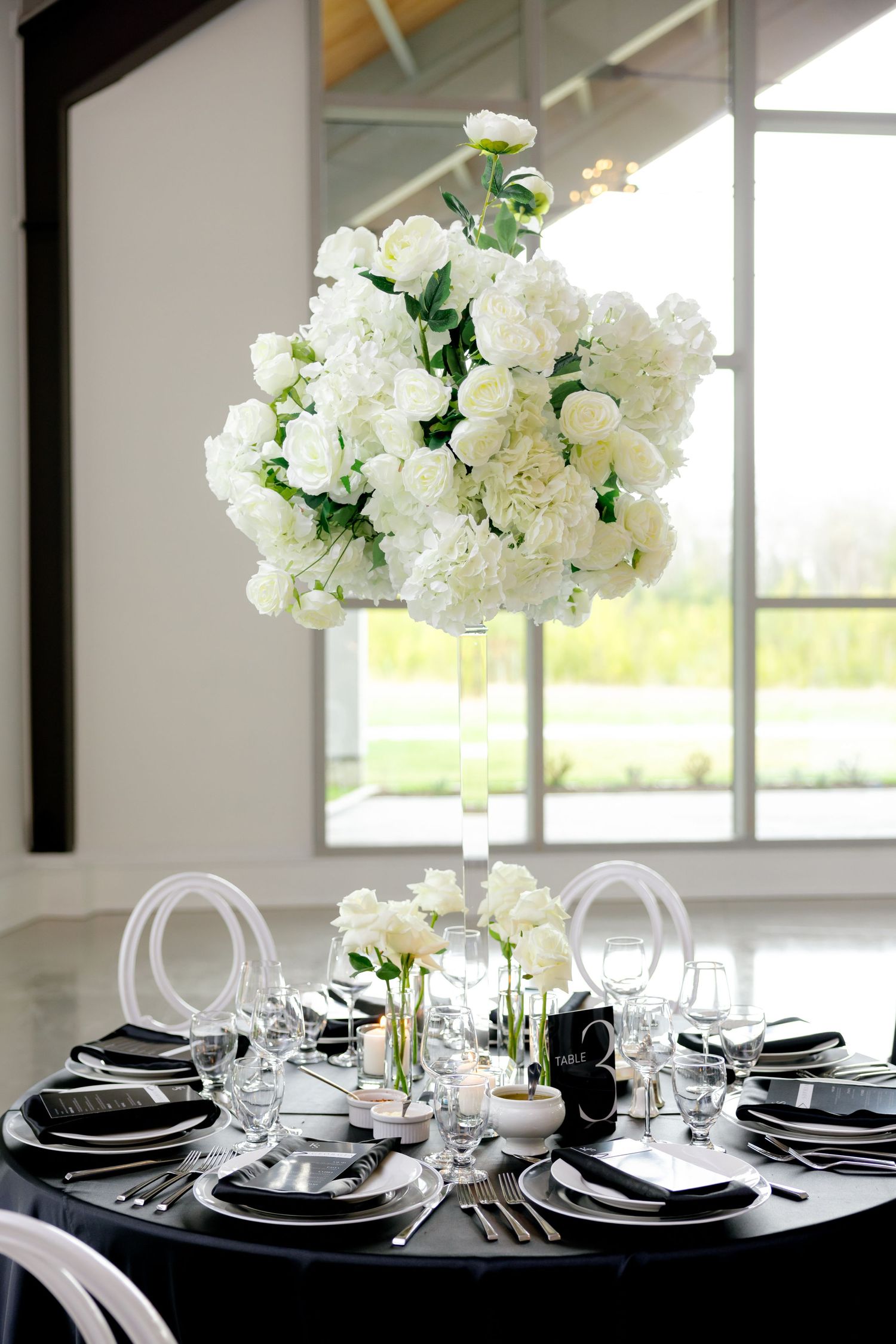 Round table with black linens and white floral centerpiece in modern venue with large windows.