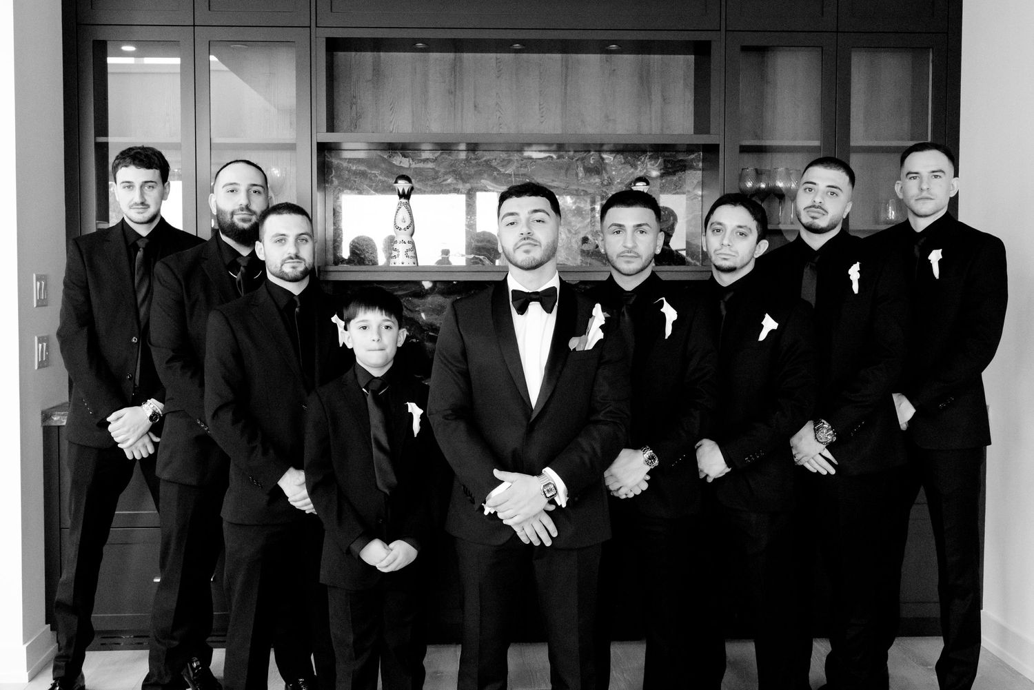 A formal black and white portrait of groomsmen in tuxedos standing together.