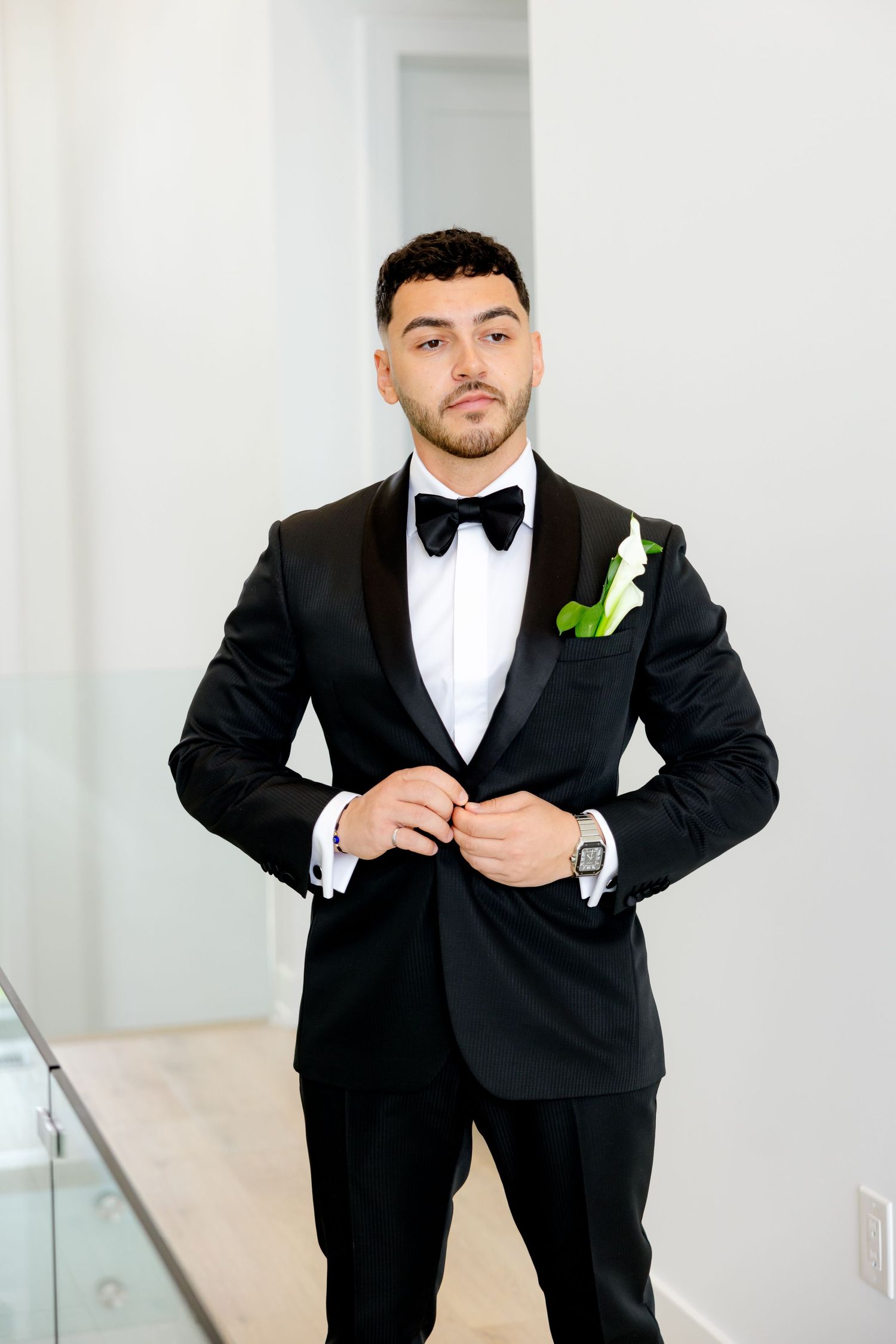 Groom in classic black tuxedo adjusts jacket while wearing boutonniere.