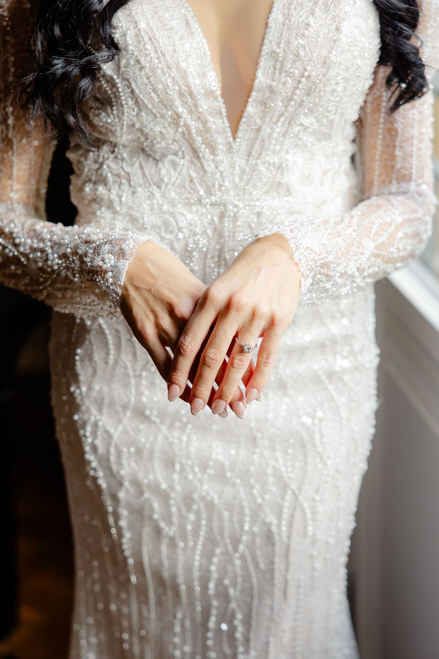 Detail shot of hands showing off rings against a sparkly white wedding gown.