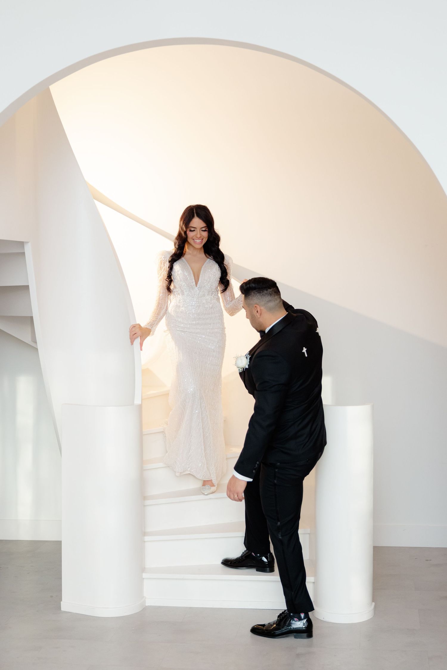 Wedding couple on modern white staircase with curved architectural details.