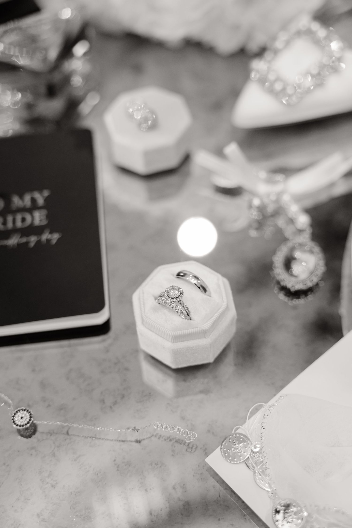 Black and white detail shot of wedding rings in hexagonal boxes with stationery.