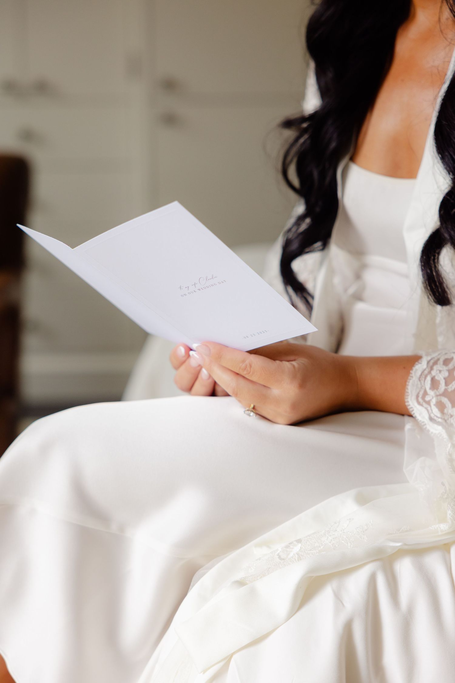Hands in white lace wedding dress holding a handwritten letter in natural light.