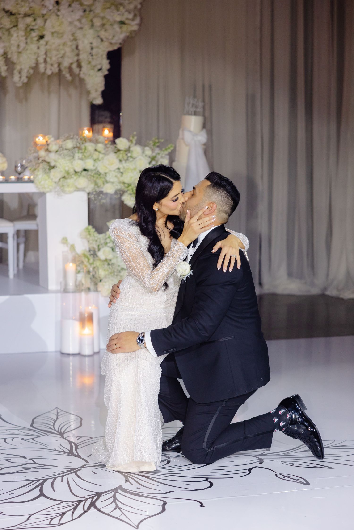 Romantic wedding moment captured on decorated dance floor with white floral backdrop.