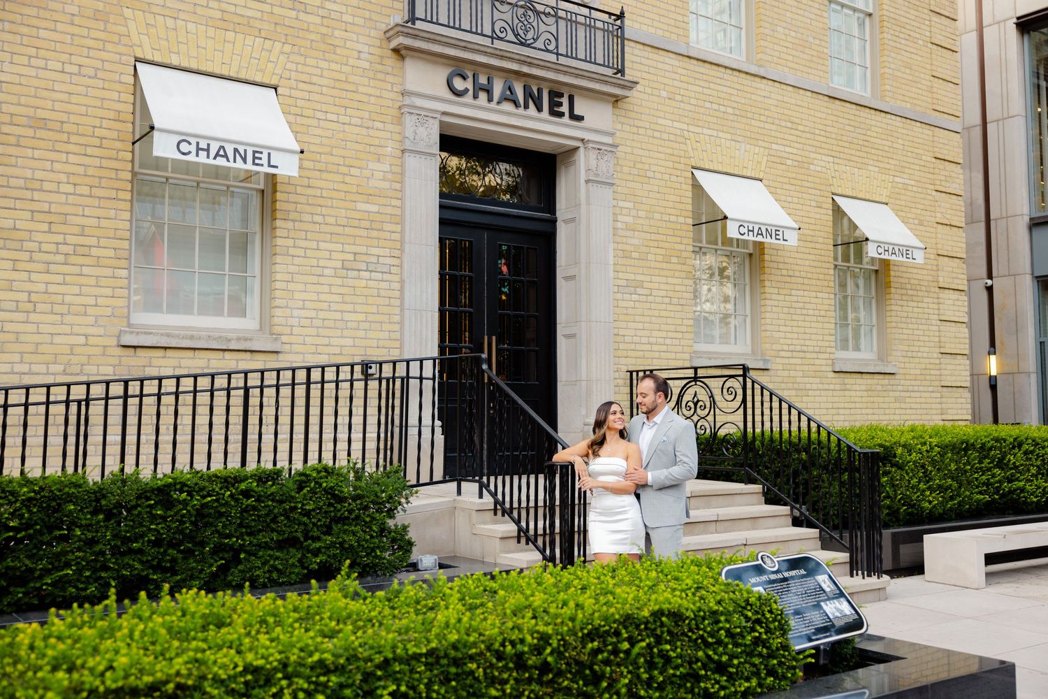 Romantic photoshoot on steps of Chanel boutique with manicured hedges in foreground.