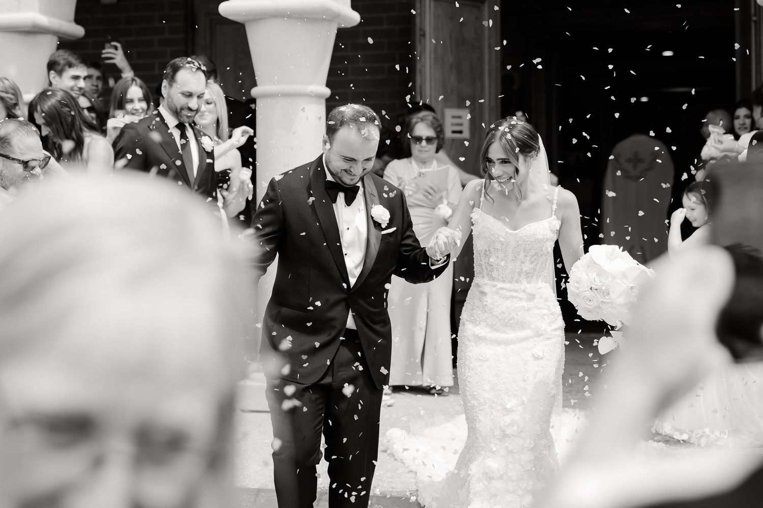 Wedding guests throw white confetti over the happy couple as they exit their ceremony in celebration.