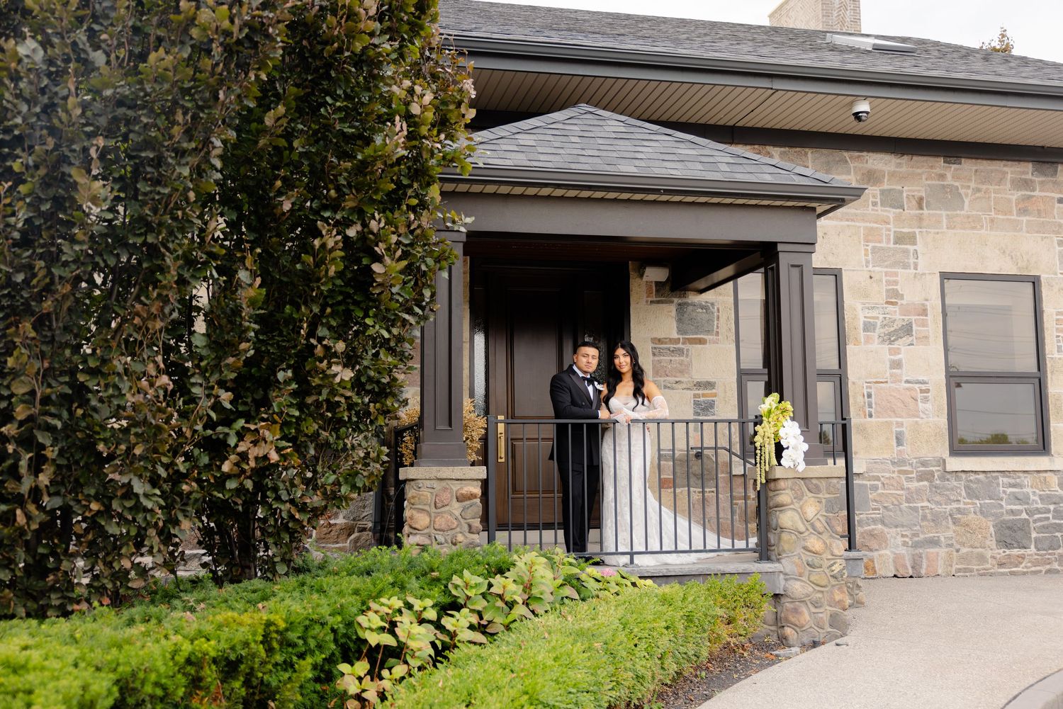 Modern stone and wood facade of a residential building features covered walkway and landscaped greenery.