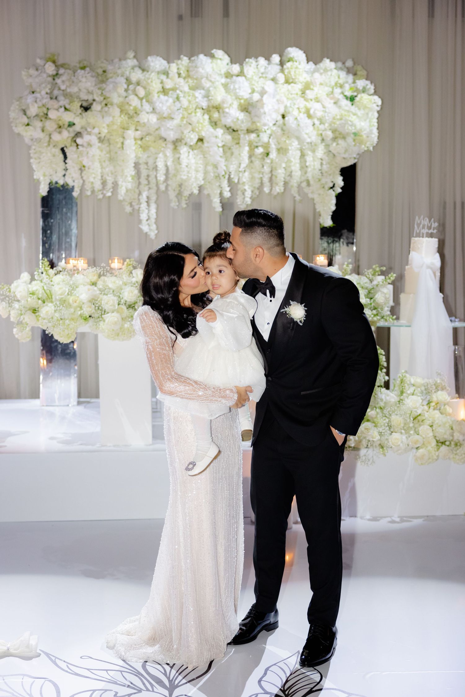Wedding party poses together under a luxurious white floral chandelier installation.