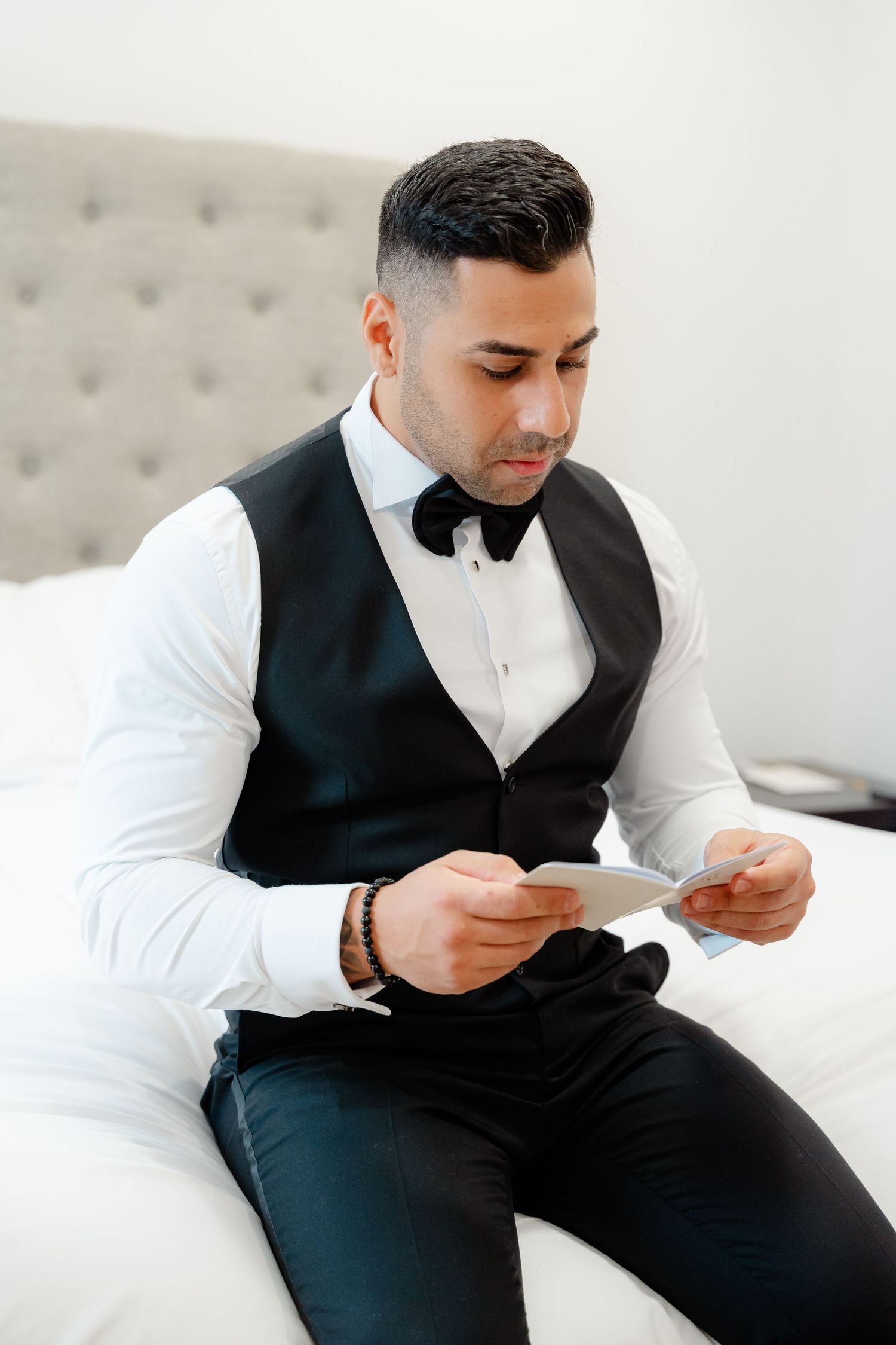 Man in formal attire reading a note while sitting on a tufted couch.