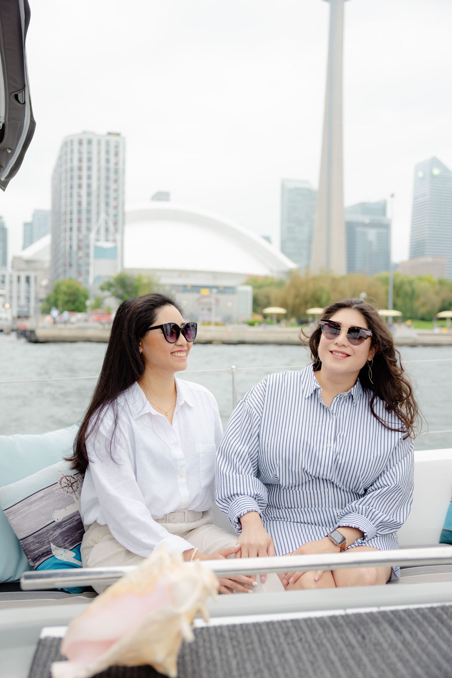 Two friends enjoying a boat ride along Toronto's waterfront with the CN Tower and Rogers Centre in the background.