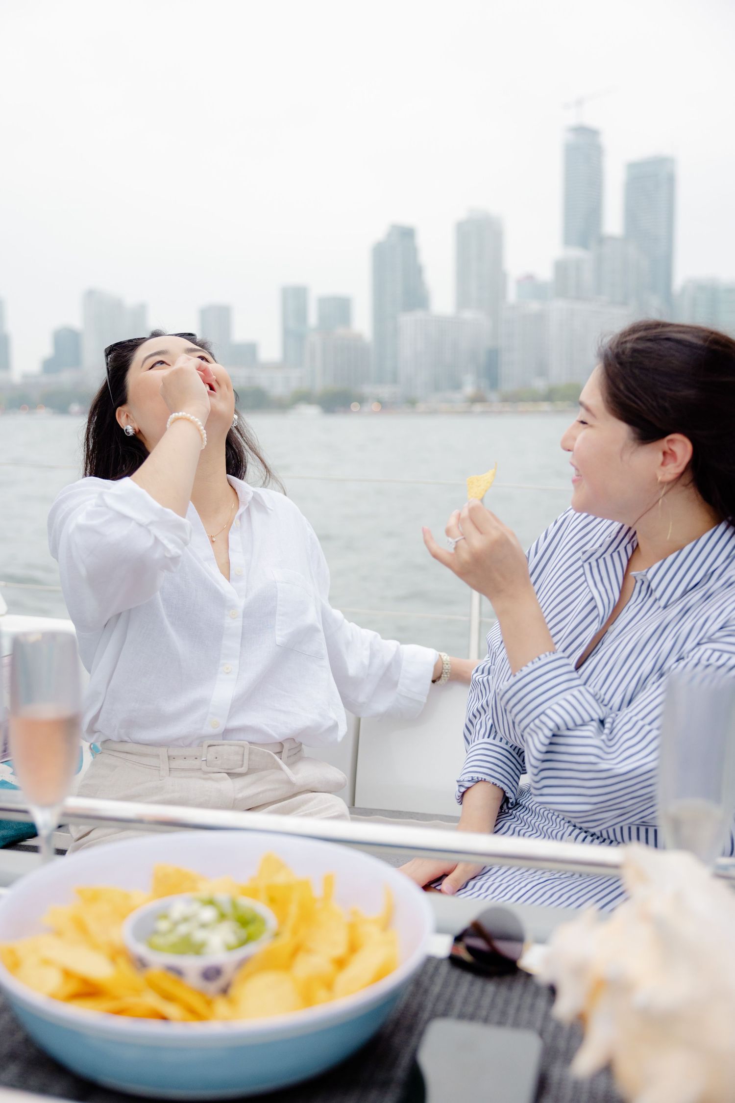 Friends enjoying snacks and drinks on a boat with Toronto's downtown skyline visible in the distance.