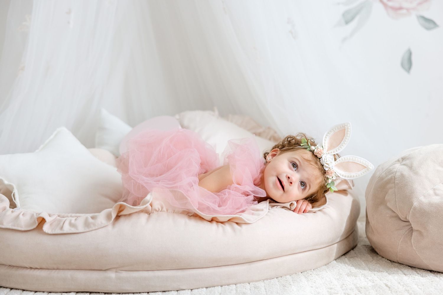 A pink tulle dress and party hat create a dreamy portrait against soft white bedding and floral decor.