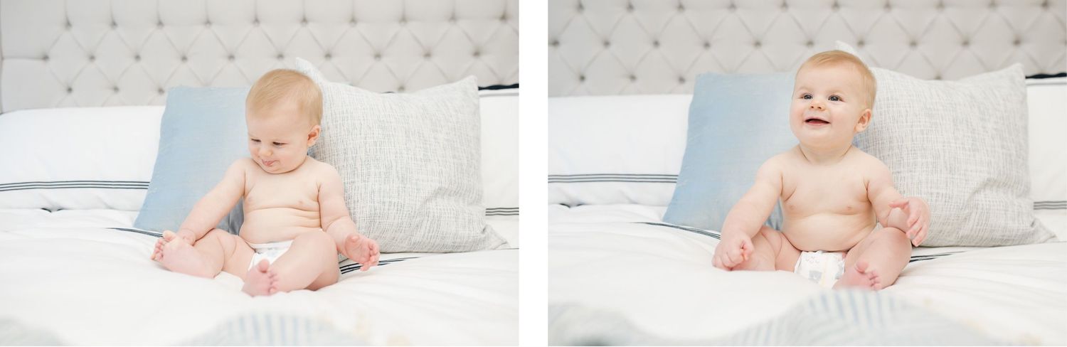 Baby in diapers sitting on white bedding with blue pillows.